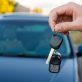 Mână care ține cheile unui autoturism, cu o mașină în fundal, imagine ilustrativă pentru închirieri auto în Iași.